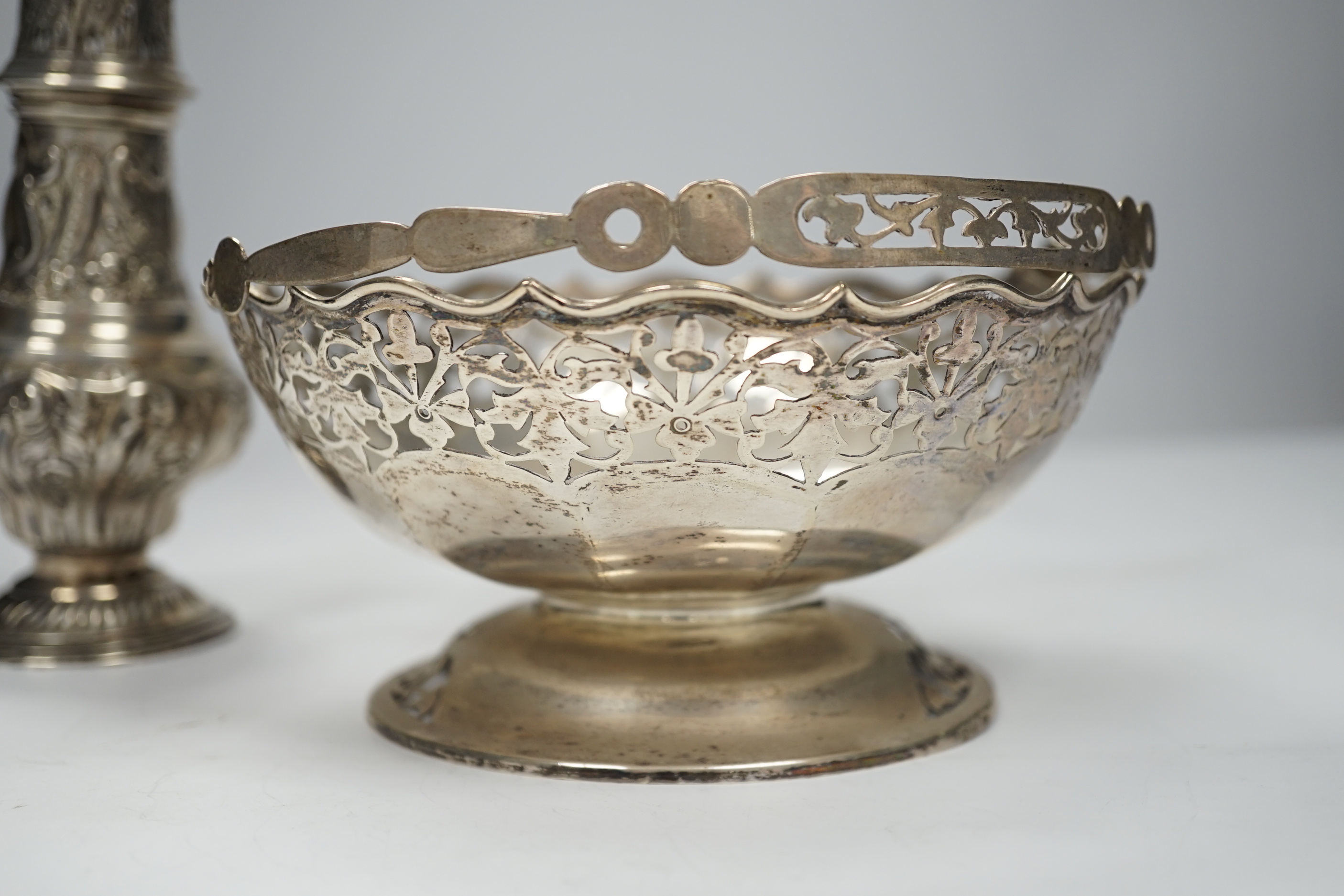 An Edwardian embossed silver sugar caster, Birmingham, 1904, 17.6cm and white metal cake basket stamped 'silver'.